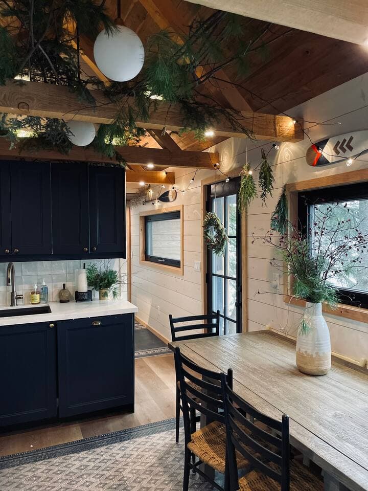 Navy kitchen and rustic wood dining table festooned with greenery and warm string lights.