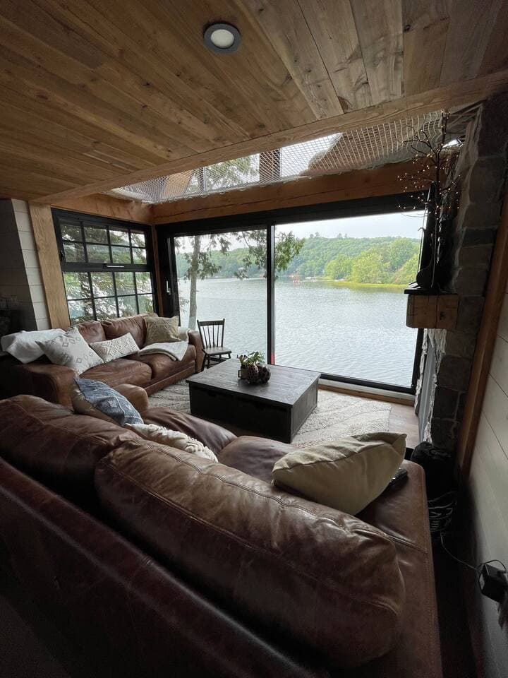 Cozy living room with deep leather sofas, wood ceiling and floor-to-ceiling lake windows.