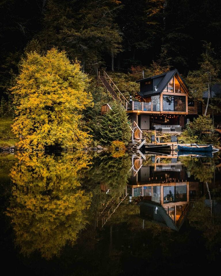 Red Adirondack chairs around a lakeside fire pit as the treehouse glows at sunset on Three Mile Lake